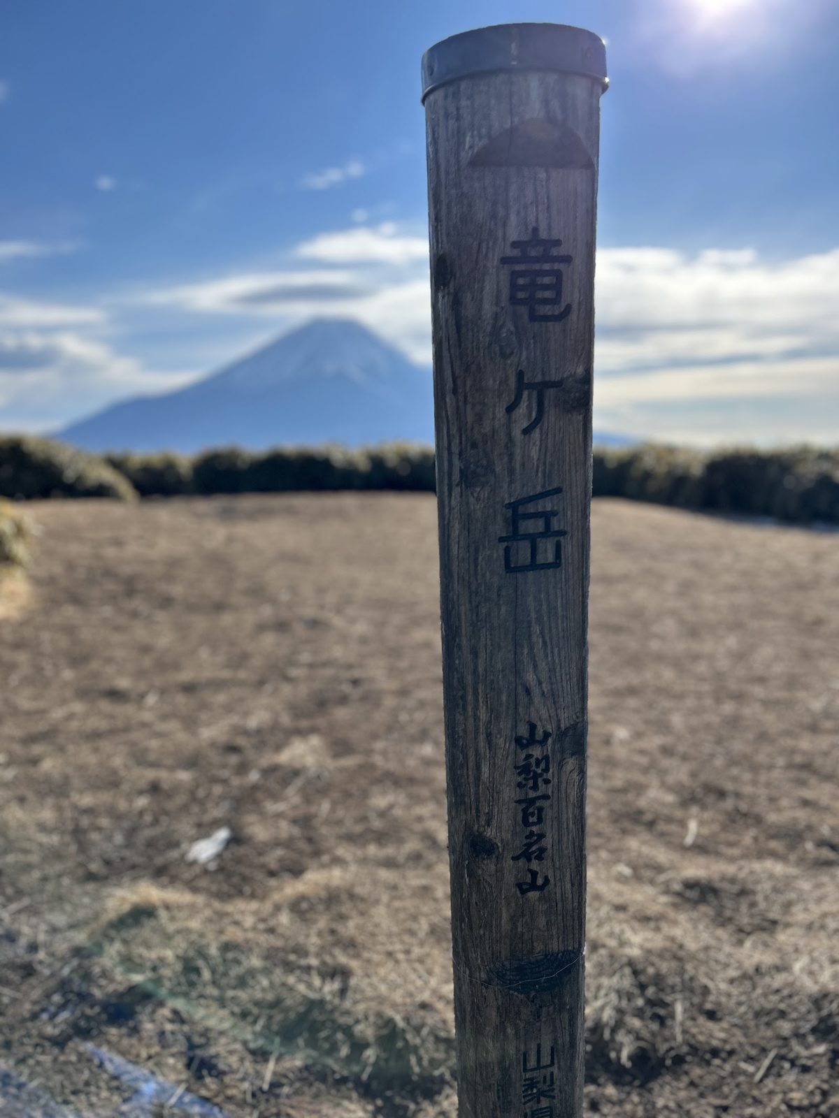 山梨・本栖湖の竜ヶ岳の山頂標識と、その奥にそびえる富士山